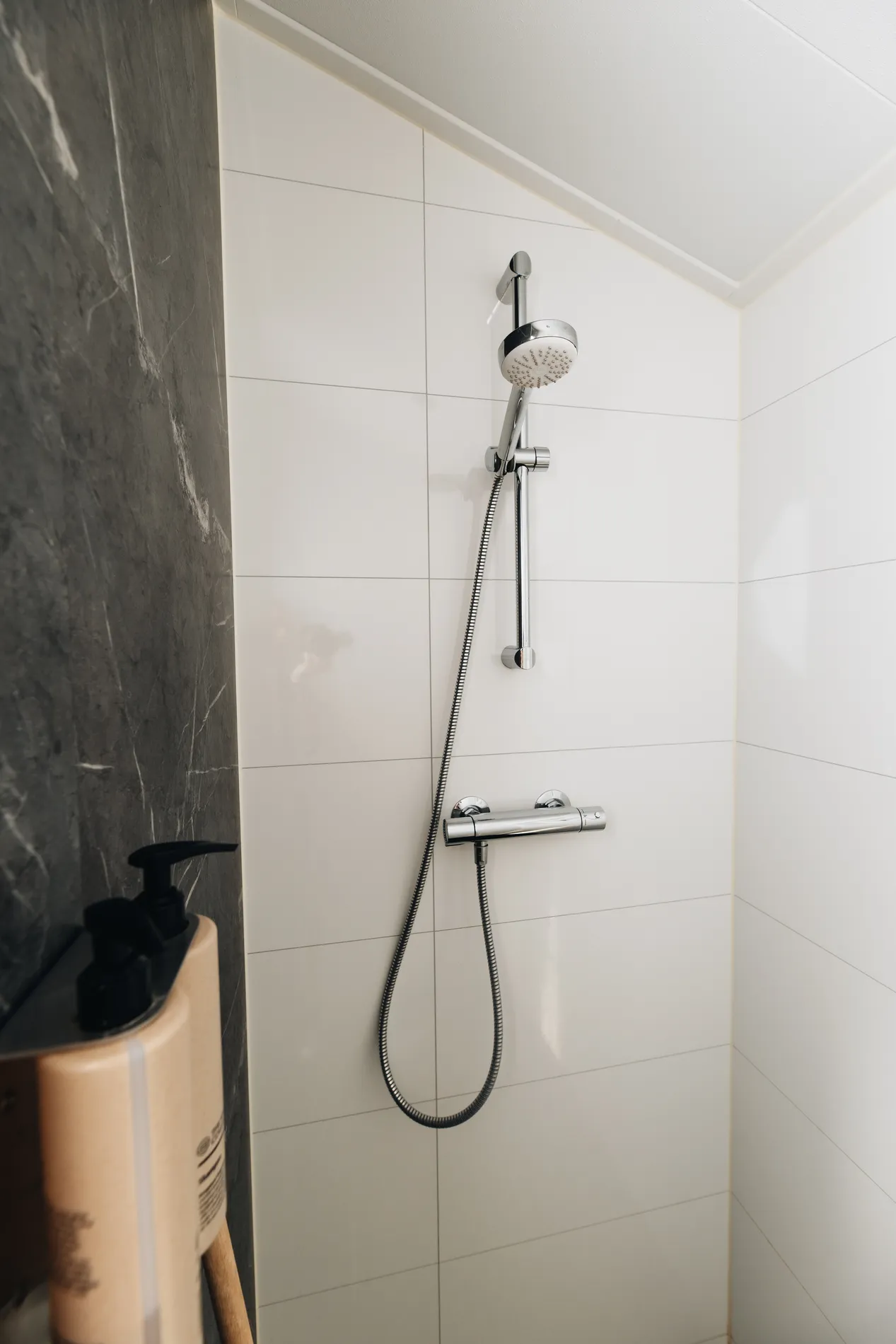 Moderne chromen doucheset tegen een strakke witte tegelwand in de badkamer van het resort.